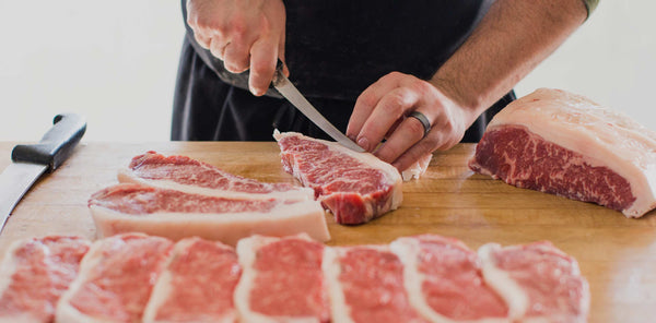 Hands trimming marbled steak on butcher block